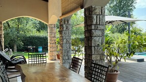 Un patio al aire libre con mesa y sillas de madera, pilares de piedra y vista a follaje.