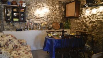 A stone-walled room with a dining table set for two, a floral sofa, and a shelf with various items.