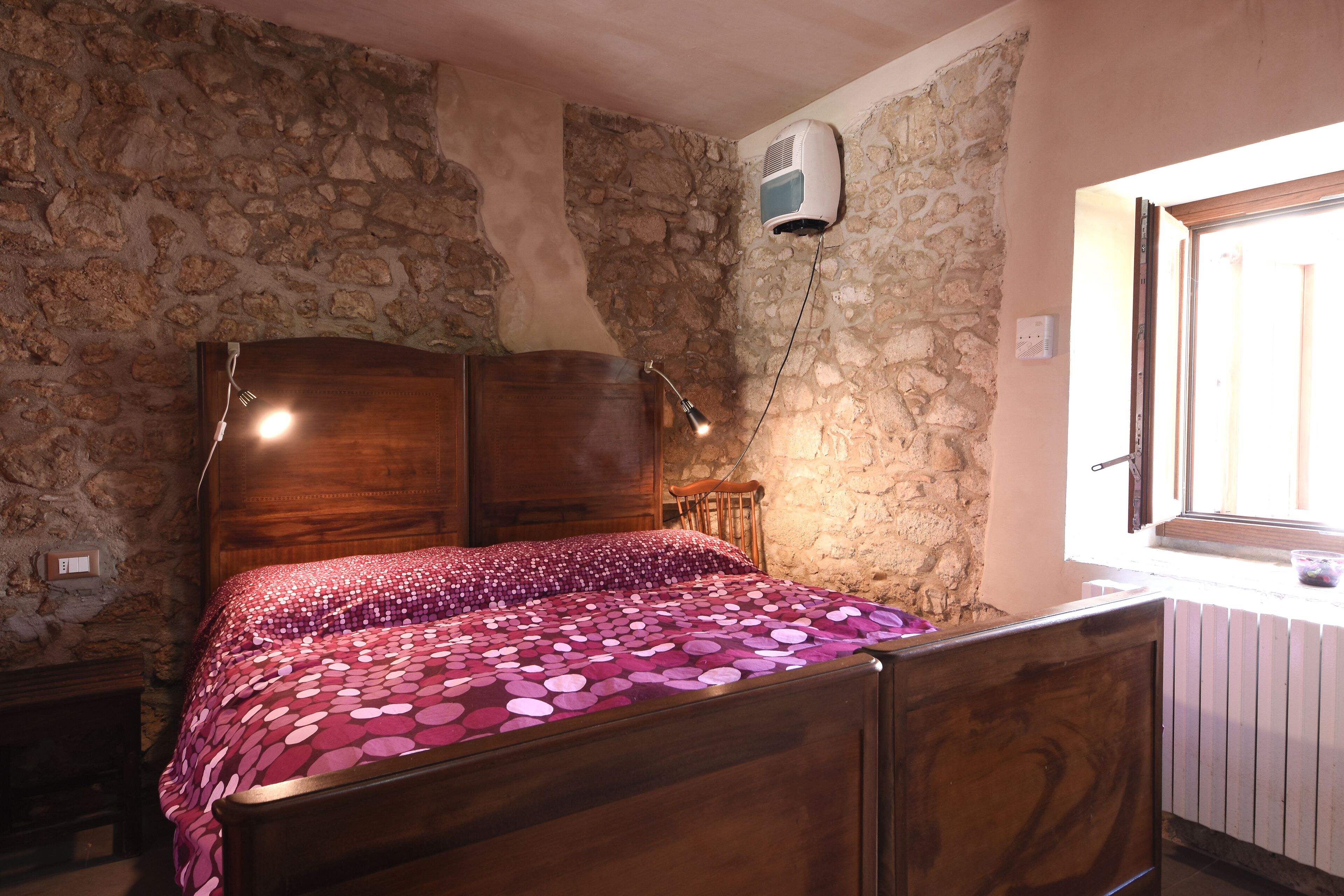 Una camera da letto con un letto di legno, pareti in pietra, una finestra e una ventola a soffitto.