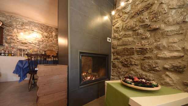 Ein gemütlicher Raum mit Steinwand, Kamin, Essbereich mit Stühlen und Tisch sowie einer Bar mit Flaschen.