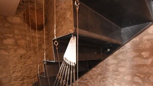 Eine Wendeltreppe mit einer Steinwand im Hintergrund, Metallgeländern und einer hängenden Leuchte.