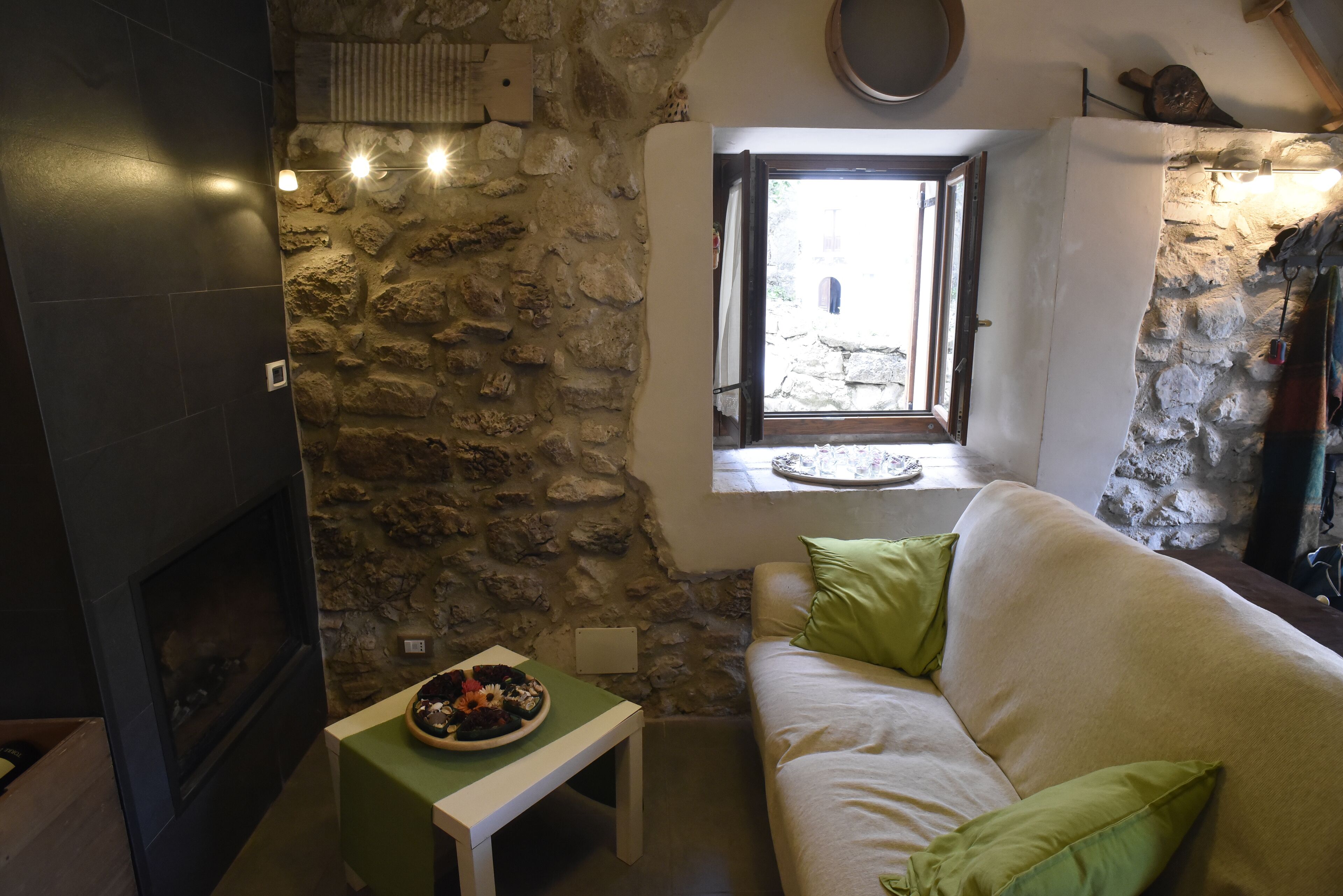 Ein gemütlicher Raum mit Steinwand, Kamin, Fenster mit Aussicht und einem grünen Tisch mit einem Teller.
