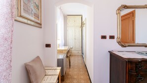 A narrow hallway with a white bench, a dining table with chairs, a chandelier, and a wooden cabinet with a mirror. - Romantic Seaview Double Room (Corniglia)