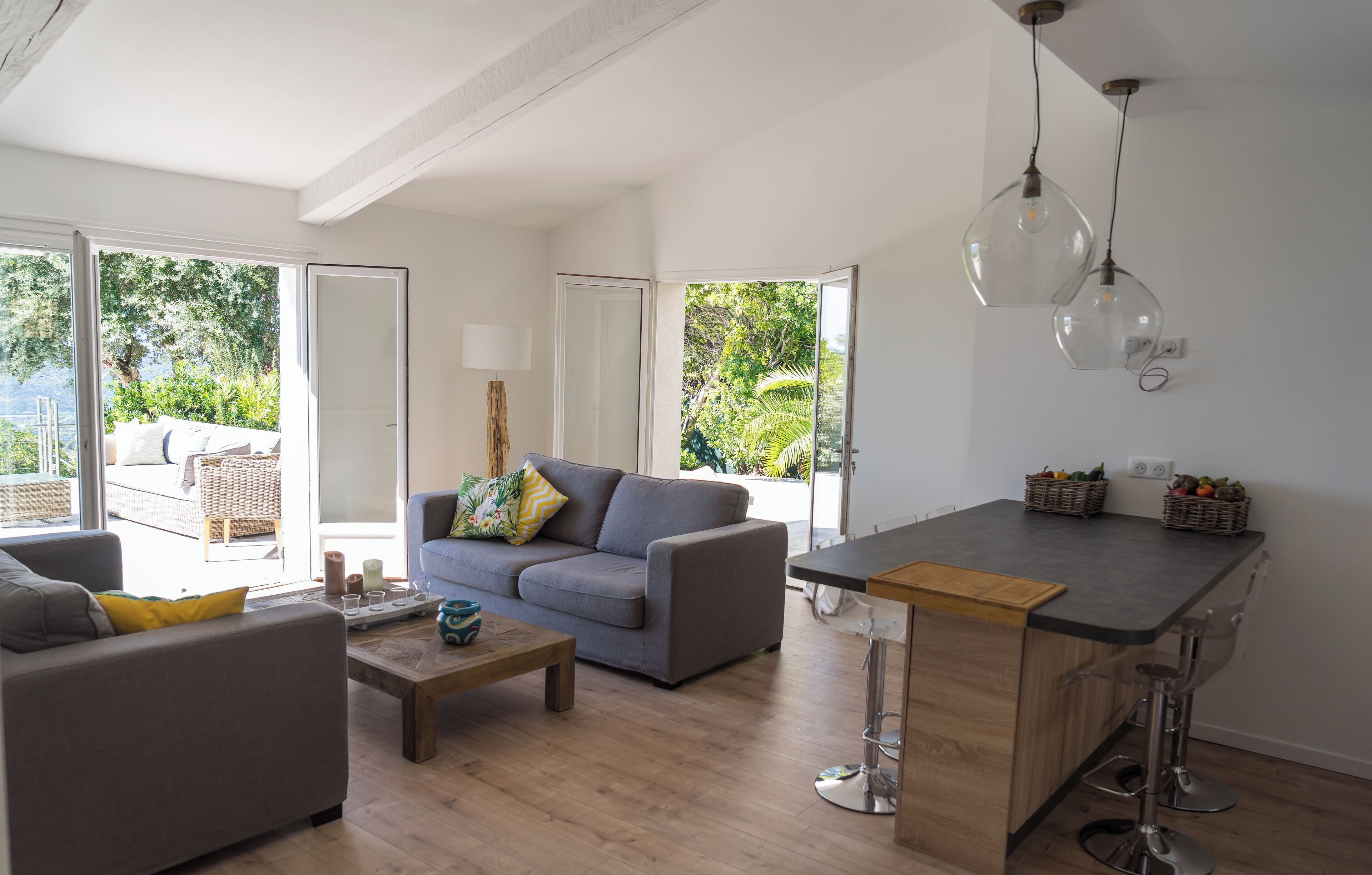 Een moderne woonkamer met een grijze bank, een houten salontafel en een keuken met een barstoel.
