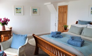 Une chambre à coucher avec un lit, une chaise, une table ornée d’un vase de fleurs et deux tableaux encadrés accrochés au mur.