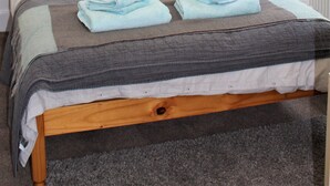 Una cama bien hecha con una manta a rayas gris y blanca, almohadas grises y toallas dobladas.