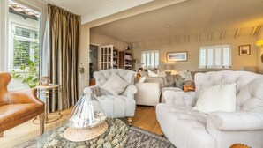 A spacious living room with a large window, a fireplace, and a comfortable seating area. - Whitehaven, Brancaster, Norfolk (King's Lynn)