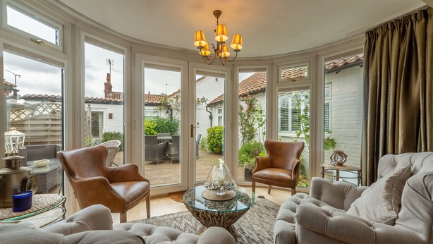 A spacious living room with a glass coffee table, leather armchairs, and a view of the backyard through large windows. - Whitehaven, Brancaster, Norfolk (King's Lynn)