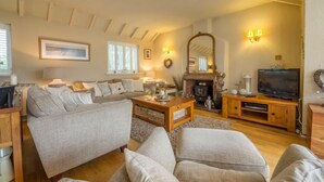 A cozy living room with a sofa set, a fireplace, a television, and a wooden coffee table. - Whitehaven, Brancaster, Norfolk (King's Lynn)
