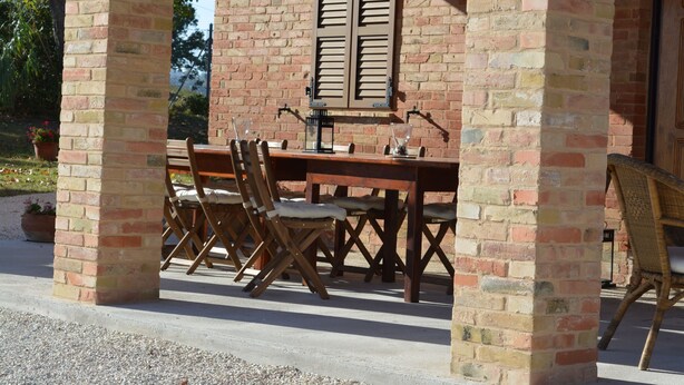 An outdoor patio with a brick wall, wooden table, and chairs. - Franca's House (Sant'Angelo in Pontano)