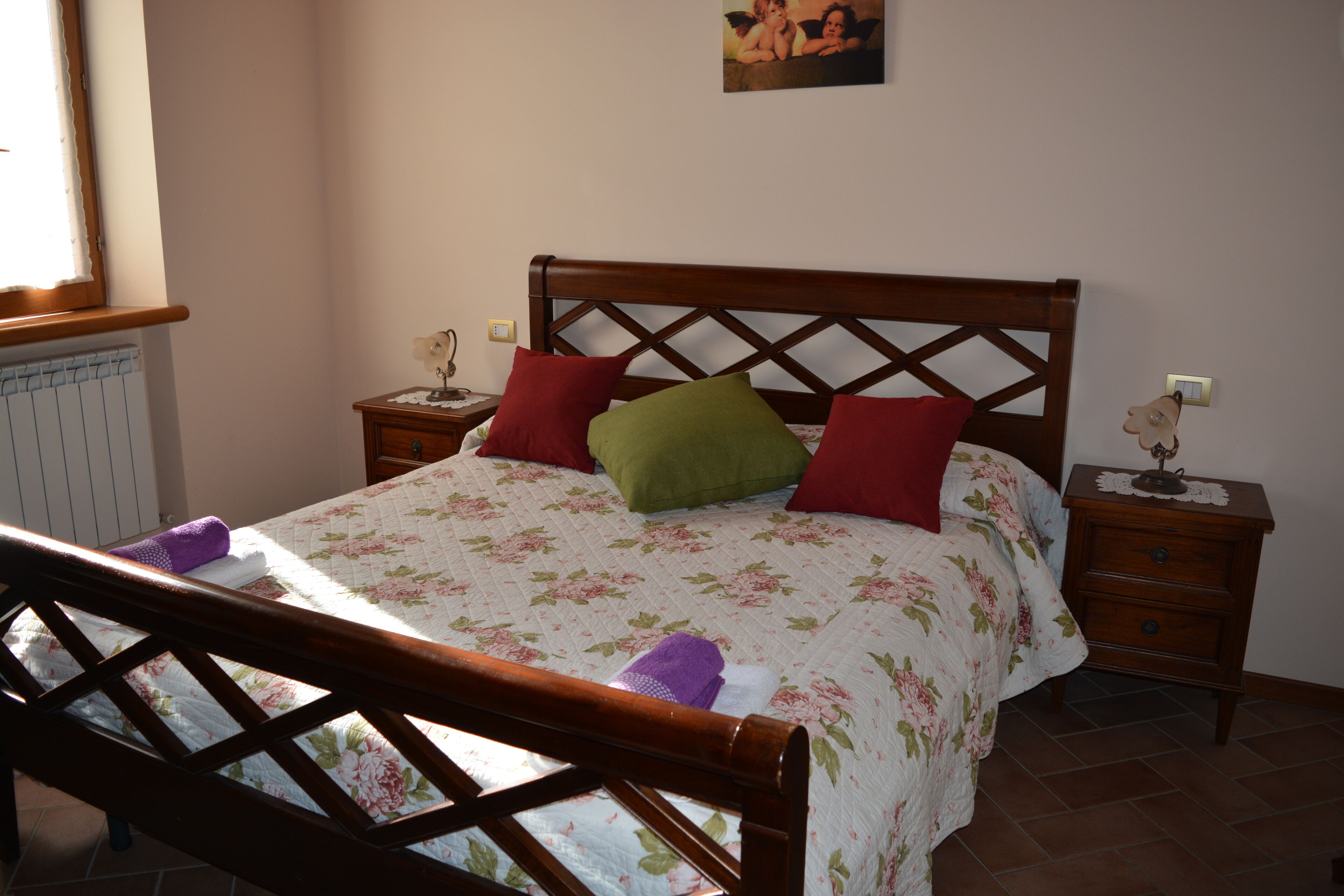 Een netjes opgemaakt bed met bloemenbeddengoed, een houten hoofdbord en twee nachtkastjes met lampen.