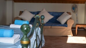 A bedroom with a bed, a wooden headboard, a blue towel, a beige sofa, and a fan. - Franca's House (Sant'Angelo in Pontano)