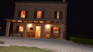 A two-story house with a brick facade, multiple windows with shutters, and a covered porch area with outdoor seating. - Franca's House (Sant'Angelo in Pontano)