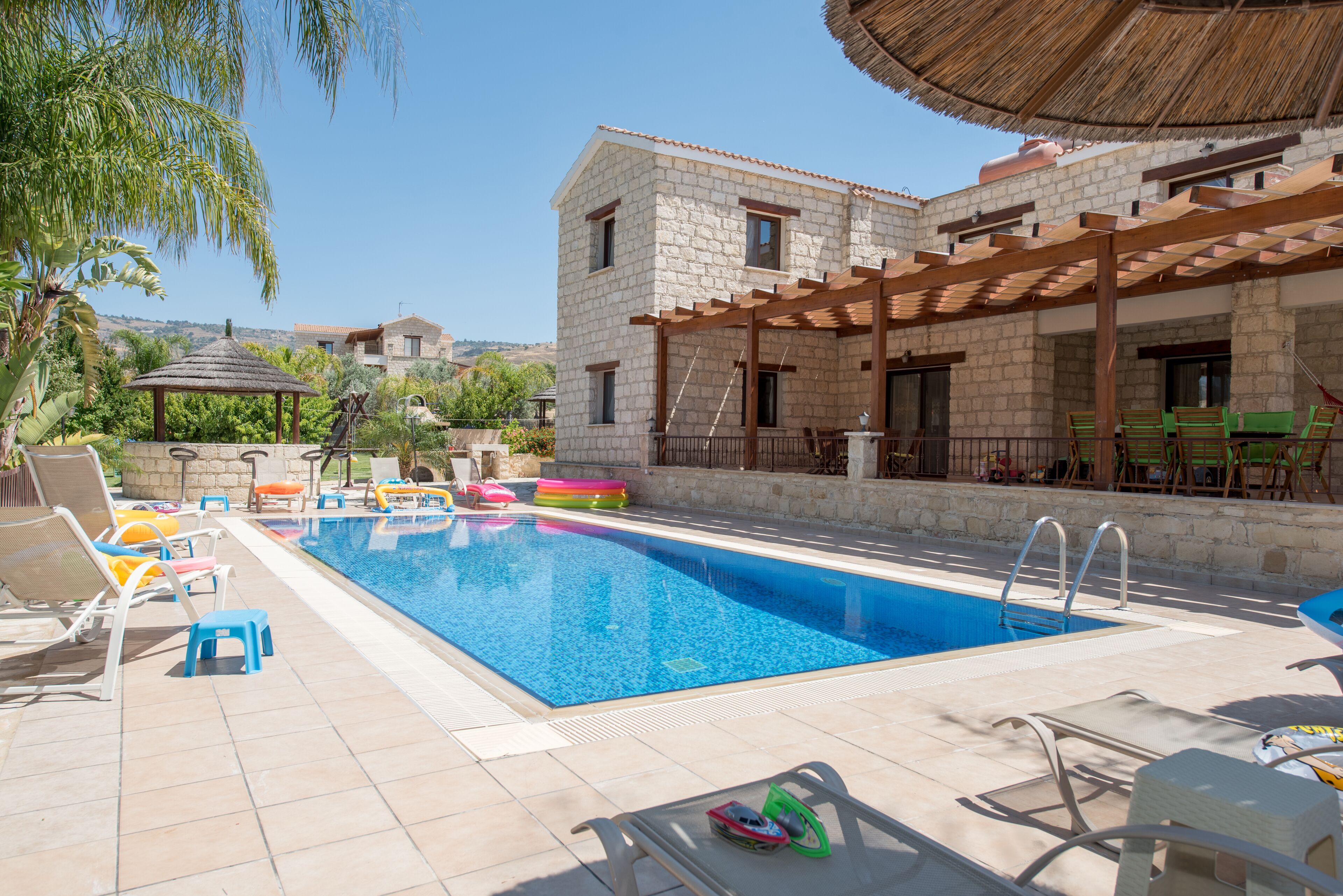 Una piscina con sillas de descanso y una pérgola, rodeada de edificios de piedra.