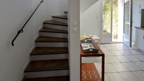 A staircase with wooden steps and black handrails, leading to a room with a tiled floor and a small wooden table.