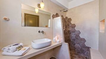 Un baño con un espejo grande, un lavabo blanco, una ducha con pared de piedra y una toalla con bolsitas de lavanda.