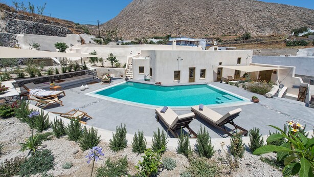 Uma área de piscina com espreguiçadeiras e montanhas ao fundo.
