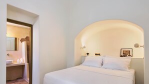 Quarto com cama branca, mesa de cabeceira branca e luminária fixada na parede.