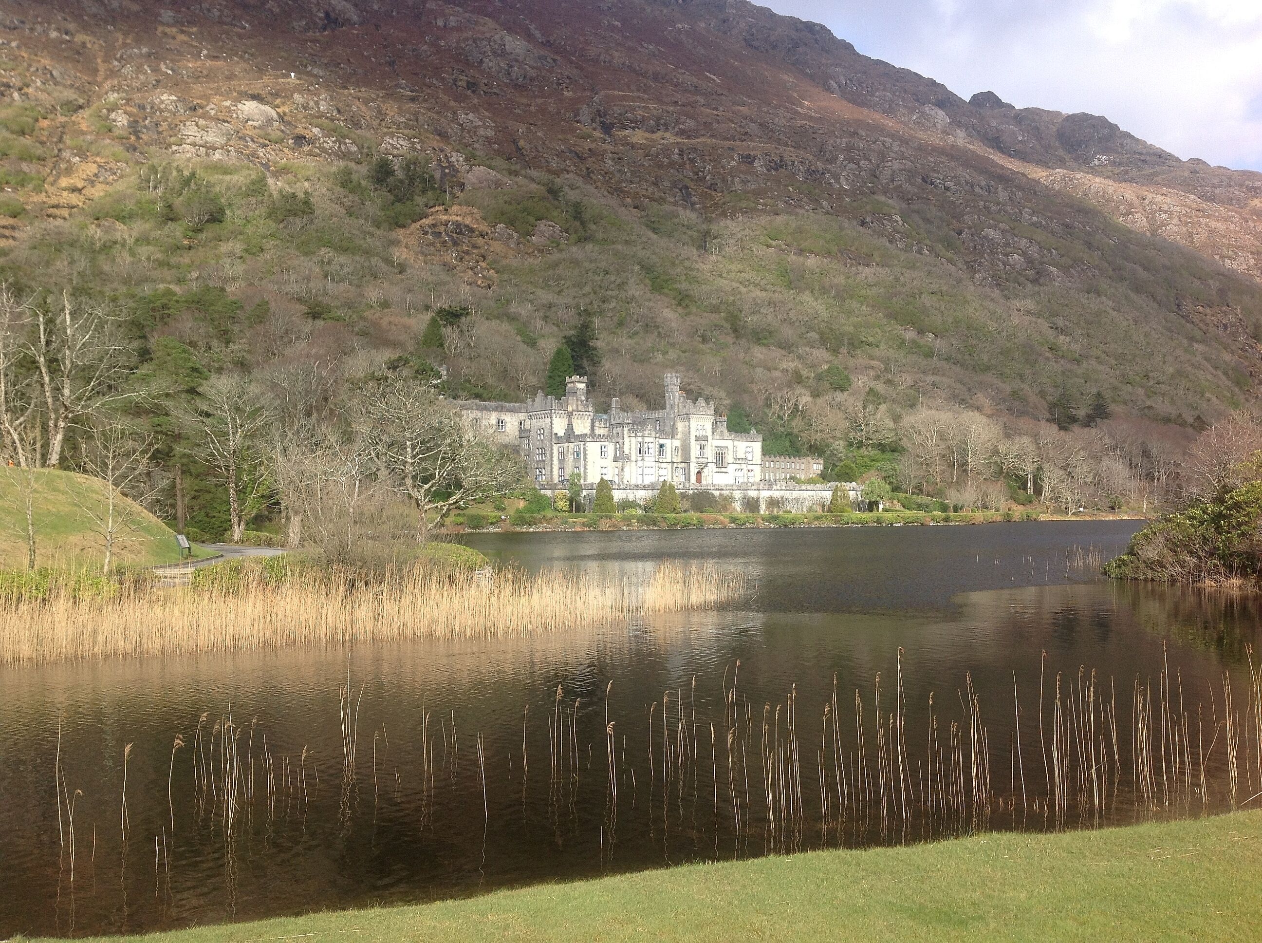 A historic building with a lake in the foreground and a mountainous backdrop.