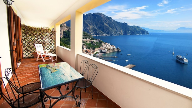 Un balcon avec une table et des chaises, offrant une vue sur la côte, avec des montagnes et la mer.