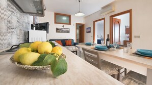 Une cuisine moderne avec un long plan de travail, un saladier rempli de citrons et un coin repas avec une table mise pour quatre personnes.