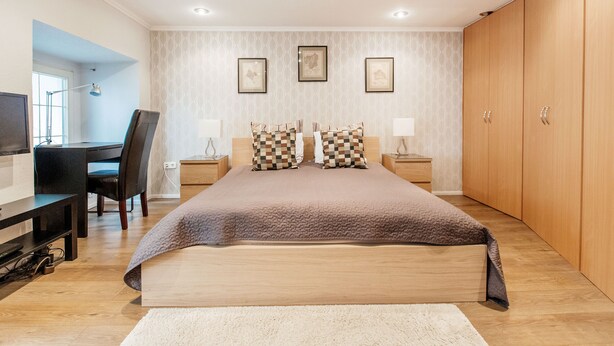 A bedroom with a bed, bedside tables, a desk, and a TV.