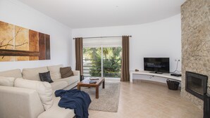 Una sala de estar con sofá, mesa de centro, televisor, chimenea y vistas a través de puertas de cristal.