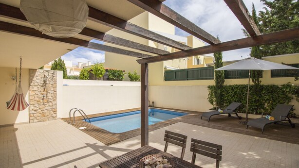 Un área de piscina con mesa, sillas y sillones de descanso.