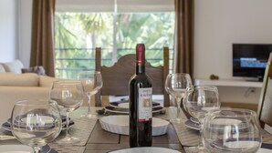 Mesa de comedor dispuesta con copas de vino, platos y una botella de vino en una habitación con vista a espacios verdes.
