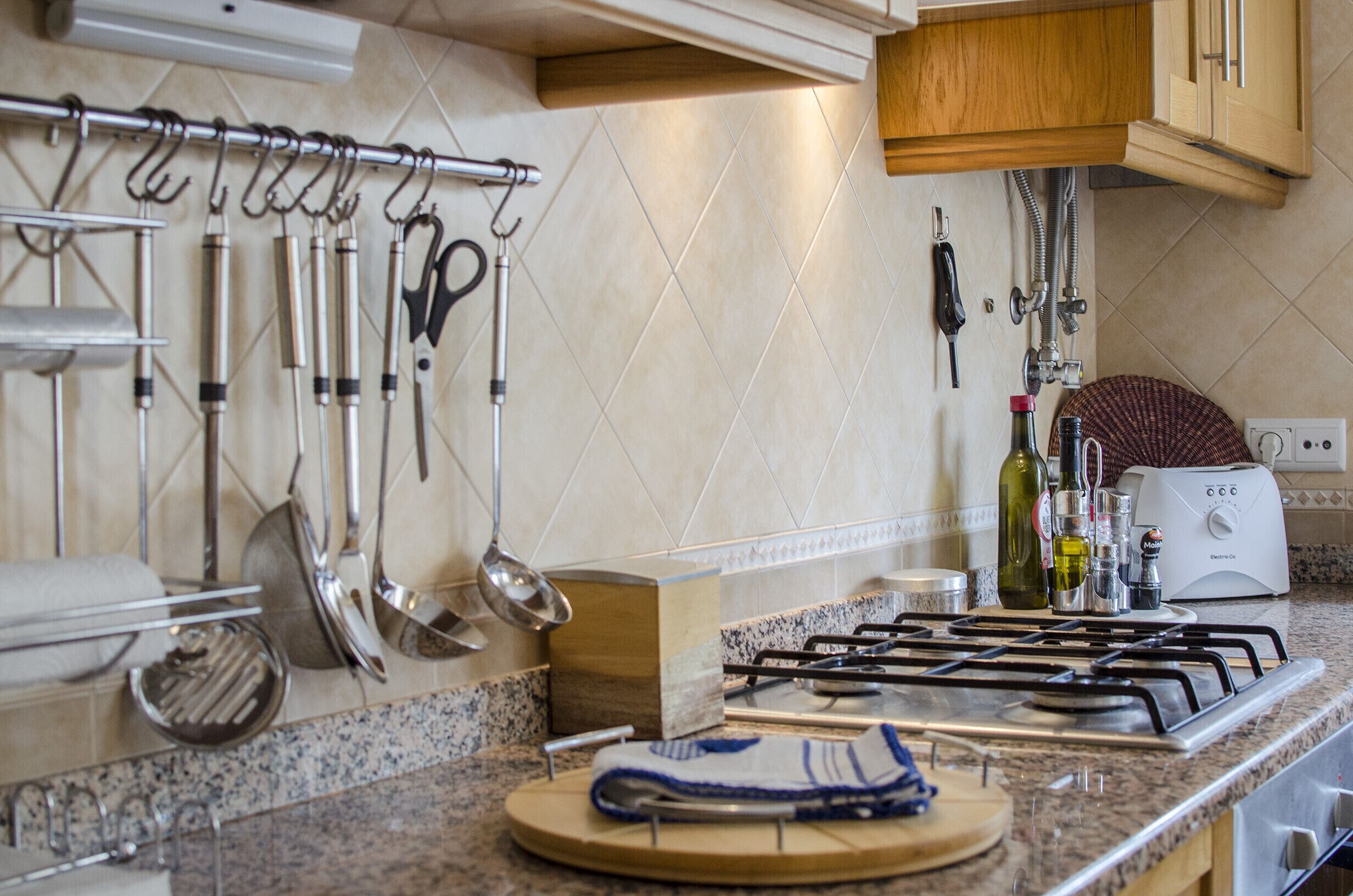 A kitchen with a gas stove, hanging utensils, and a toaster.