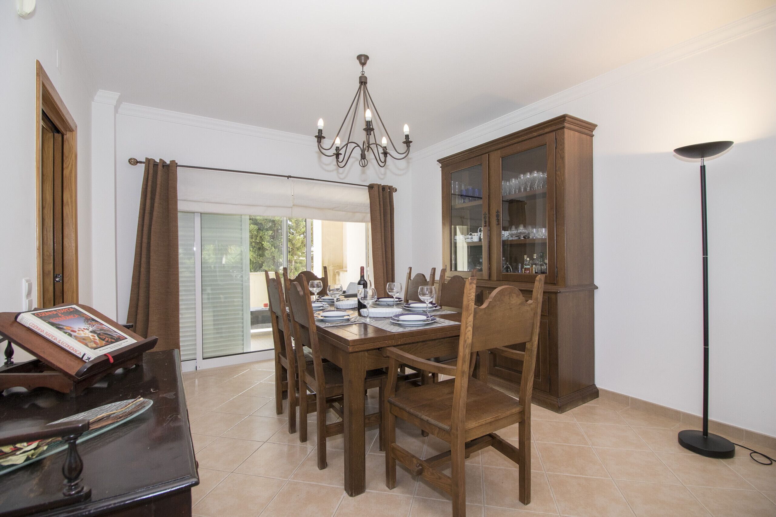 A dining area with a wooden table set for six, a chandelier, and a cabinet with glass doors.