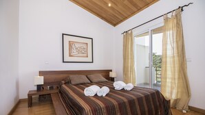 Un dormitorio con cabecera de madera, una cama con colcha a rayas, dos lámparas de noche, un cuadro enmarcado en la pared y una ventana con cortinas.