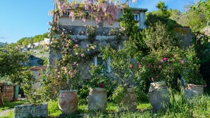 Ein rustikales Gebäude mit Naturstein-Fassade, Kletterrosen und Blumentöpfen vor der Fassade.