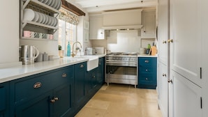 Een keuken met blauwgroene kastjes, een roestvrijstalen fornuis en een wit aanrecht.