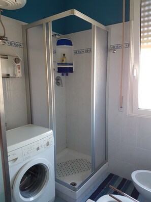 A compact bathroom with a washing machine, a shower enclosure, and a toilet.