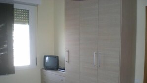 Ein Schlafzimmer mit Bett, Kleiderschrank, Fernseher und einem Fenster mit Jalousien.