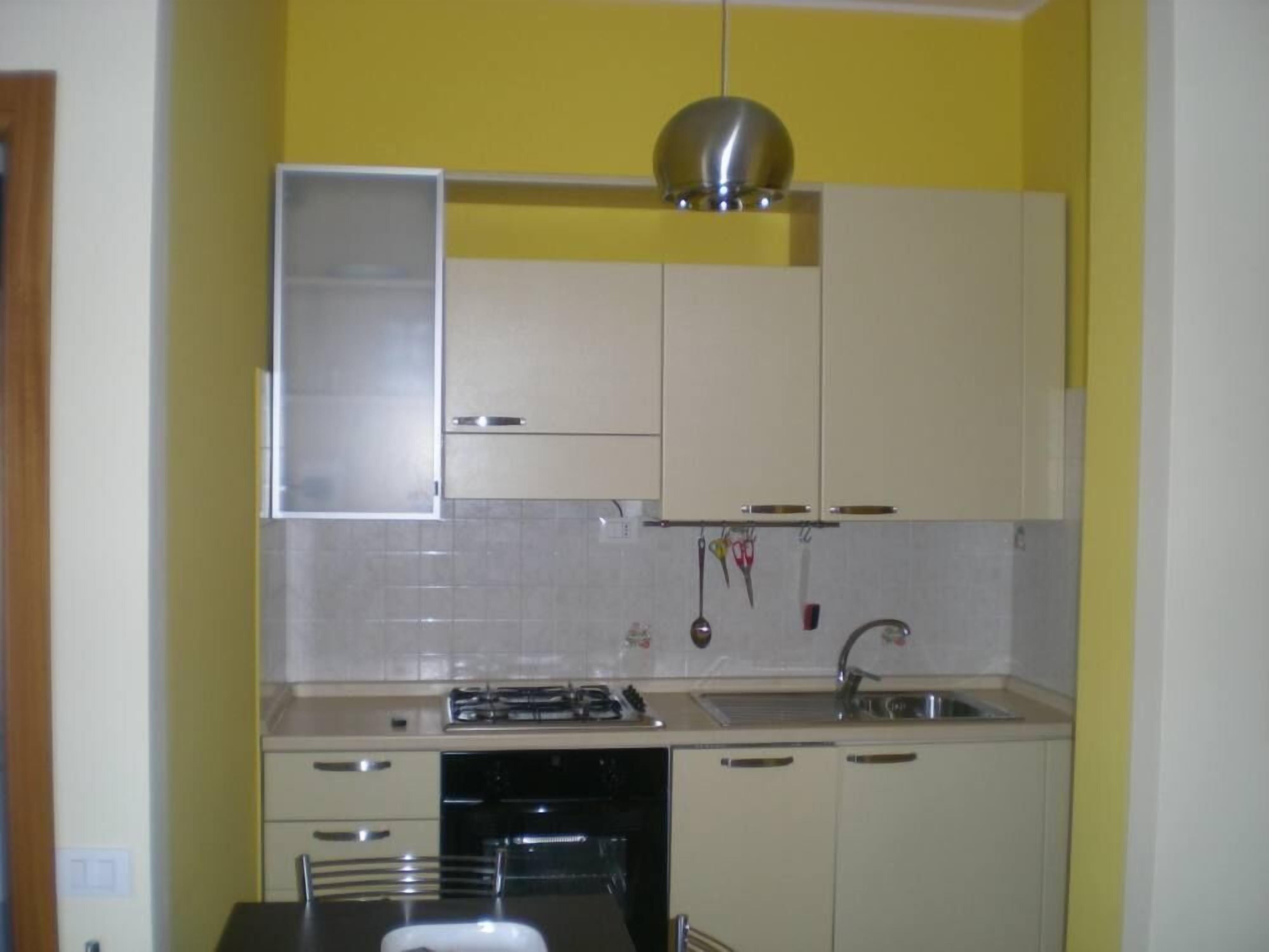 Une cuisine avec des armoires de couleur beige, un évier en acier inoxydable et une cuisinière à gaz.