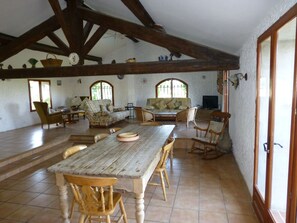 A spacious room with a wooden table, chairs, a sofa, and a television.