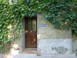 A rustic building with a wooden door, a nameplate reading 'CONSTANTIA,' and a stone wall partially covered by ivy.