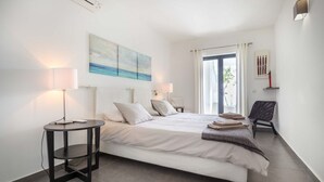 A modern bedroom with a large bed, two bedside tables with lamps, a chair, and artwork on the walls. - Beco do Poço - Praia da Luz (Luz)