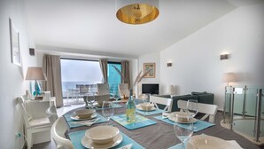 A dining area with a table set for four, a sofa, a TV, and a view of the sea. - Beco do Poço - Praia da Luz (Luz)