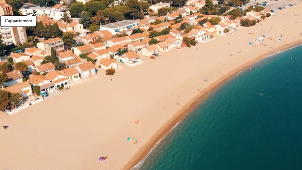 Vista aerea di una cittadina costiera con spiaggia, case e un cartello con la scritta 'L'appartement'.