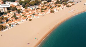 Vista aérea de un pueblo costero con playa, casas y un letrero que dice 'L'appartement'.