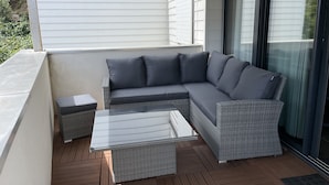 Un balcone con un divano in rattan grigio, un tavolino in vetro e un piccolo tavolino laterale.
