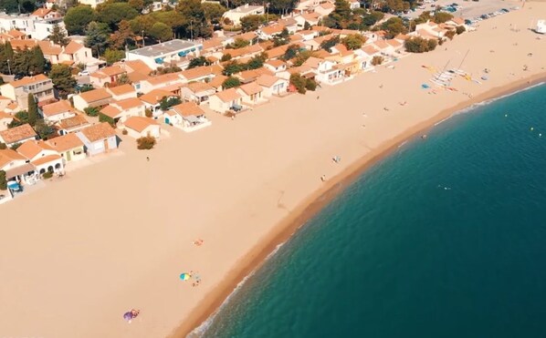 Vue aérienne d’une ville côtière avec une plage, des maisons et une enseigne indiquant « L’appartement ».