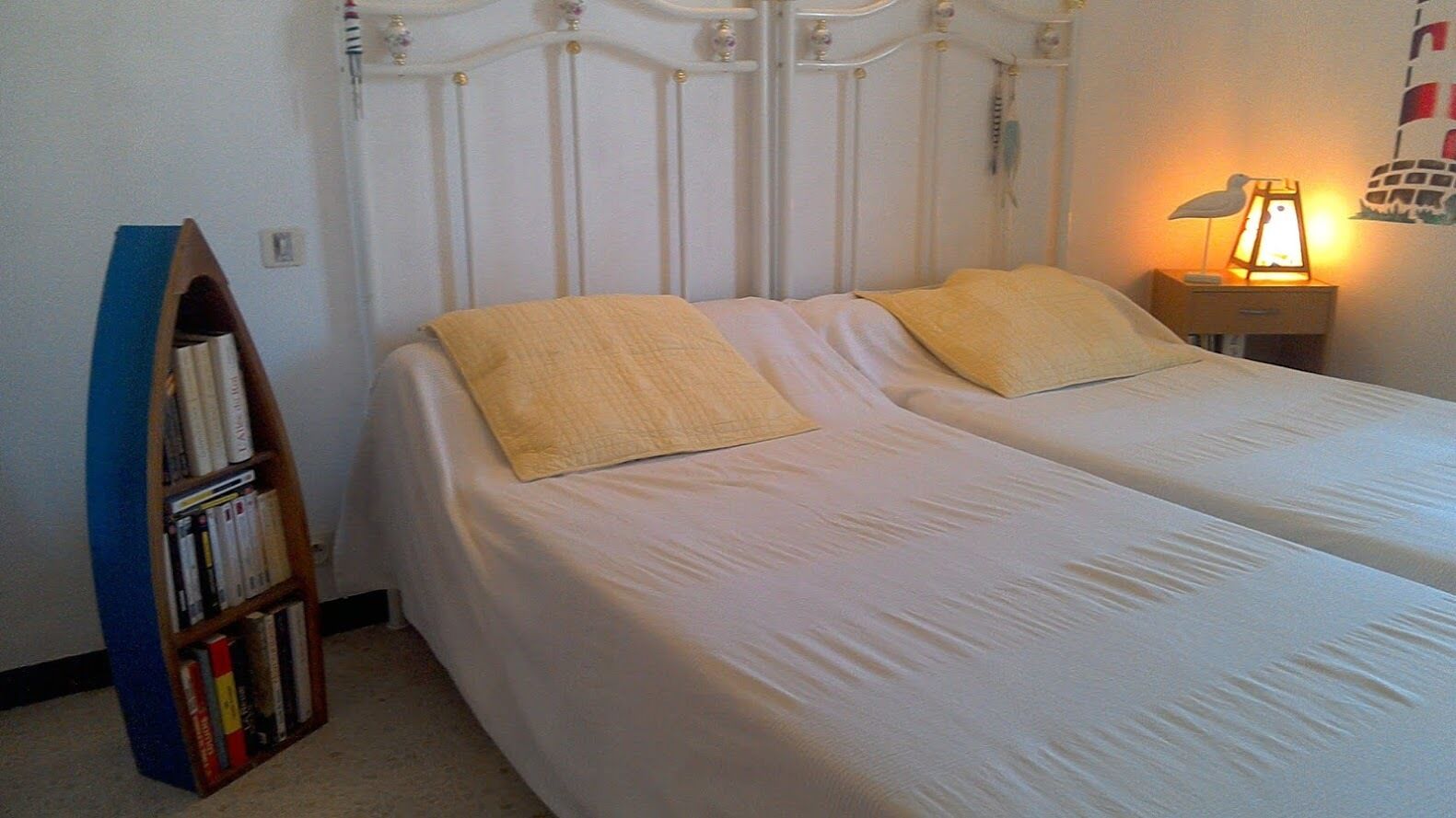 A bedroom with two single beds, a bookshelf, a nightstand with a lamp, and a wall decoration.