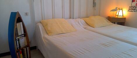 A bedroom with two single beds, a bookshelf, a nightstand with a lamp, and a wall decoration.