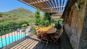 Een houten terras met een zwembad, zitgedeelte buiten en uitzicht op een berg.