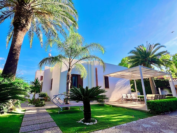 A modern building with a covered patio, a lawn, and palm trees.
