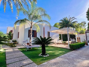A modern outdoor patio area with a pergola, seating, and a well-maintained lawn.